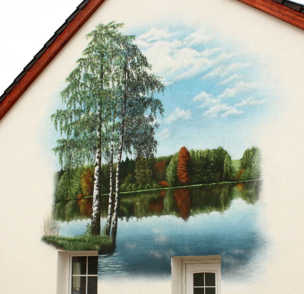 gesprühtes Graffiti auf einem Hausgiebel mit dem Motiv eines ruhigen Sees und drei großen Bäumen Birken auf einer kleinen Insel